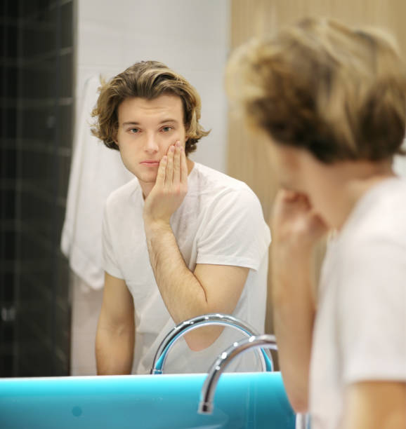 istock young man looking in the mirror,combing his hair,looking at problems on face 1203932600
