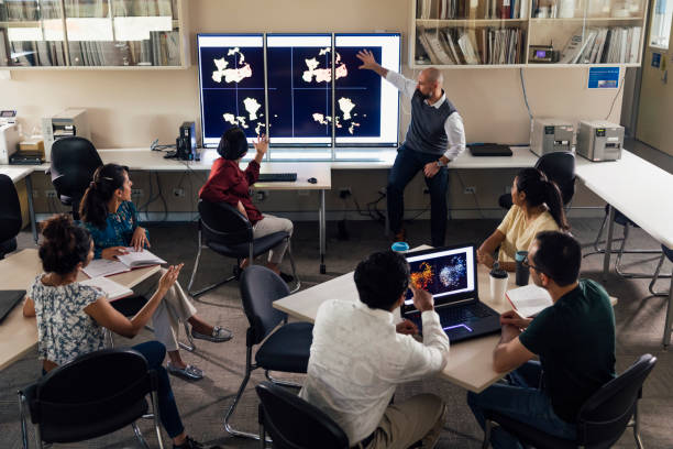 Presentation in Science Technology Classroom with Mature Students A mature man can be seen pointing to scientific matters on three large screens at the front of a classroom. There are six mature students in the room watching the presentation. university students australia stock pictures, royalty-free photos & images