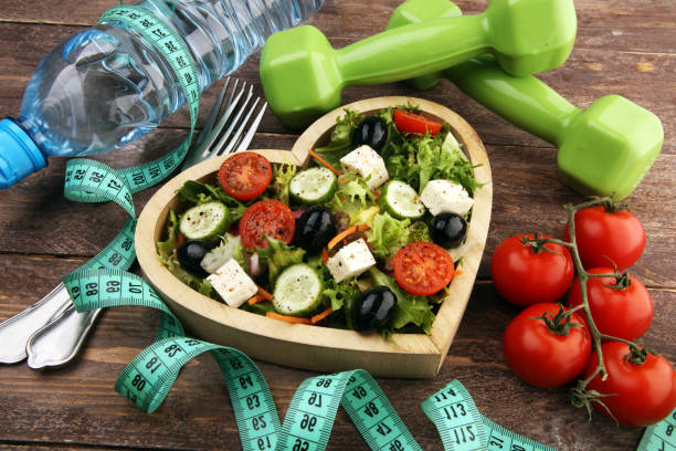 istock Authentic fresh salad in a wooden heart shaped cup with dumbbells excercise equipment, measuring tape on table. healthy lifestyles, good health 1203939621