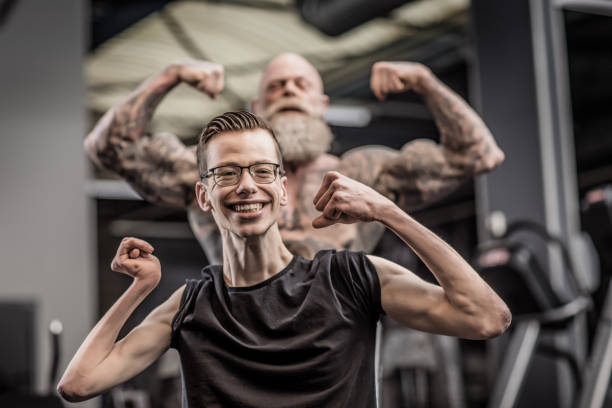 Tattooed Senior Man coaching disabled young athlete during Gym Workout Bearded paternal muscular tattooed Senior Man coaching physically challenged disabled young male athlete during indoor workout in a modern gym senior bodybuilders stock pictures, royalty-free photos & images
