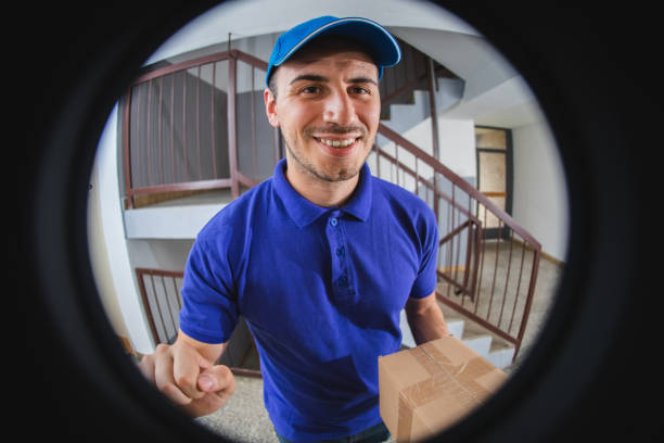 Postman with package at the door Young Caucasian man delivering package at the door. peep hole stock pictures, royalty-free photos & images