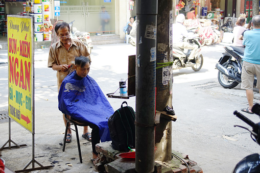 Barber cutting customer hair at the side of the road of Hanoi.