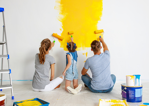 Repair in the apartment. Happy family mother, father  and child daughter    paints the wall with   paint