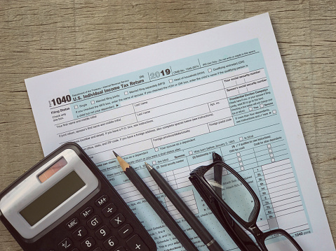 A calculator, pencil, pen, eyeglasses and featuring half of U.S IRS 1040 form. With vintage-styled background.