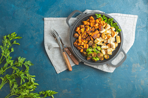 Healthy food. Pan of baking chicken meat, fried sweet potato and brussels sprouts. Top view, classic blue concrete surface, flat lay. Color of 2020 year. Classic Blue, food trendy background.