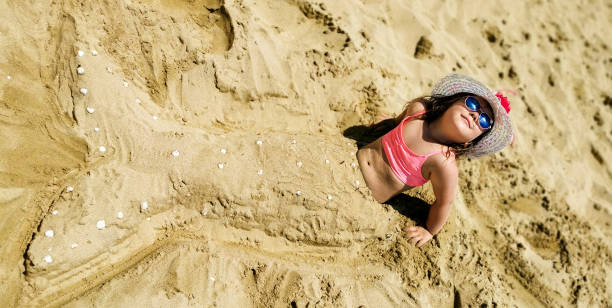 Little girl sitting on sandy beach and playing a mermaid