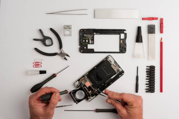 istock Man working on mobile repair, hands, with tools, screwdrivers, glue, cutting pliers, pencil and red tweezers, white background.Top view, mobile workshop concept.White background 1203959556