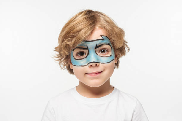 A portrait of a young boy having a mask painted onto his face.