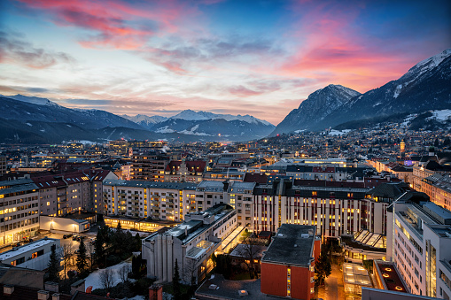 Elevated panorama of the illuminated skyline of Innsbruck in the Austrian Alps during winter dusk time with snow