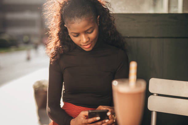 istock Black woman sitting alone in sidewalk cafe and using smart phone 1203962059