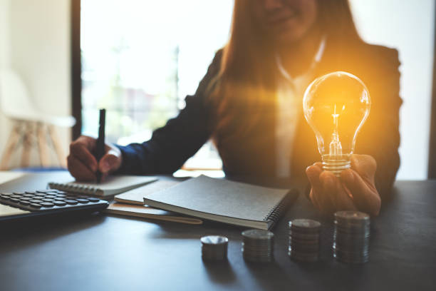 istock Businesswoman holding a lightbulb with coins stack on table 1203962150
