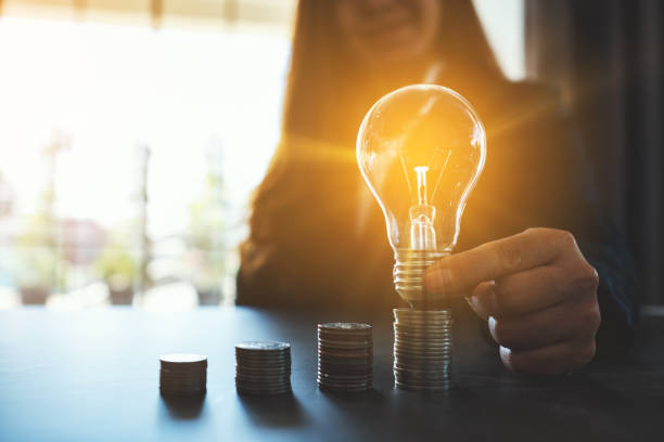 Businesswoman holding and putting lightbulb on coins stack