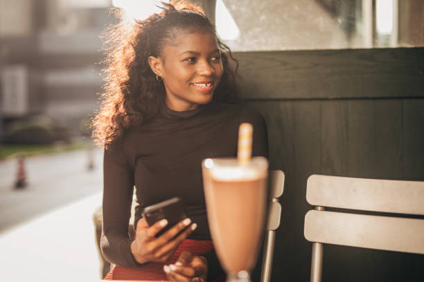 istock Black woman sitting alone in sidewalk cafe and using smart phone 1203962232