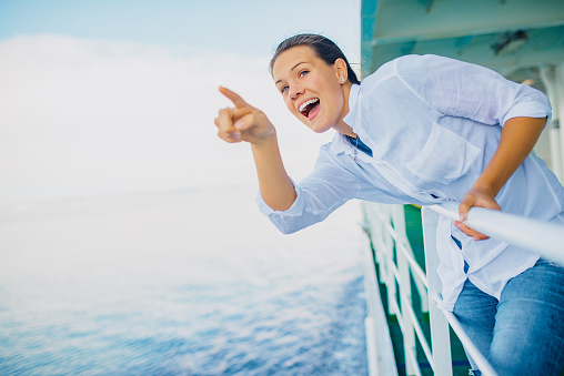 Cheerful Young Woman Pointing to the Distance from Cruise Ship