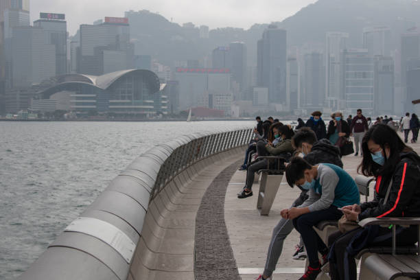 Coronavirus - Tsim Sha Tsui Promenade February 2, 2020, Hong Kong: Mask-wearing people are seen sitting at the Tsim Sha Tsui Promenade amid the COVID-19 outbreak. severe acute respiratory syndrome stock pictures, royalty-free photos & images