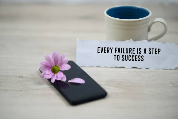 Inspirational quote - Every failure is a step to success. With morning cup of coffee and purple daisy flower on black phone on white soft blurry background. Motivational words concept.