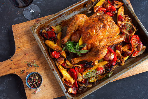 Freshly grilled roast chicken. Mediterranean preparation with vegetables and herbs on rustic wooden cutting board. Food photography lay flat with space for text. Top view.