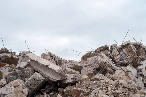 A pile of large gray concrete fragments with protruding fittings against a cloudy sky. Remnants of the destruction of a large concrete building. Building background.