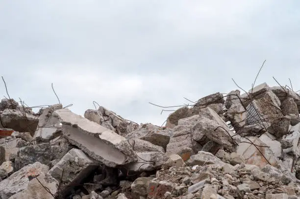 Photo of A pile of large gray concrete fragments with protruding fittings against a cloudy sky.