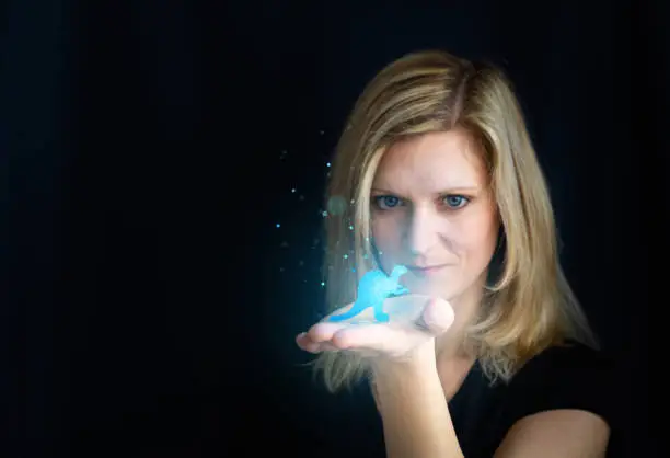Beauty young blond hair woman holding small glowing blue dinosaur, dragon. Photomanipulation glowing animal on black background