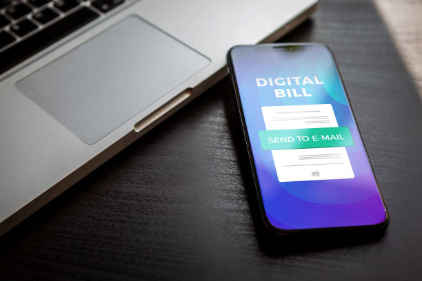 istock Digital receipt on mobile internet banking concept. Electronic digital bill or invoice on smartphone screen with a laptop in the background. Online money transaction with phone. 1203969515