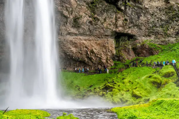 Photo of River by Seljalandsfoss waterfall long exposure in Iceland with white water and green mossy summer landscape and people walking on trail