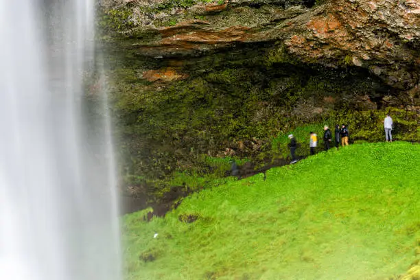 Photo of Closeup of Seljalandsfoss waterfall long exposure in Iceland with white water and green mossy summer landscape and people walking on trail