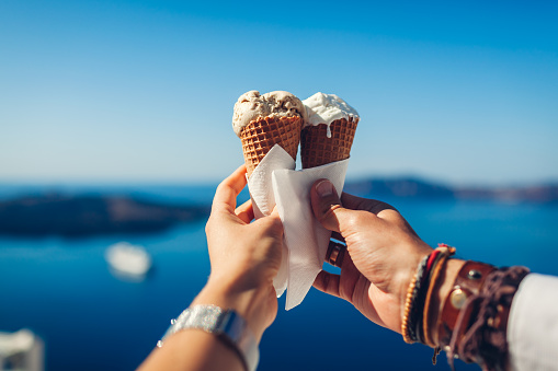 Ice-cream in cones. Couple eating ice-cream holding it on sea and islands background. Sweet tasty summer food. Close up