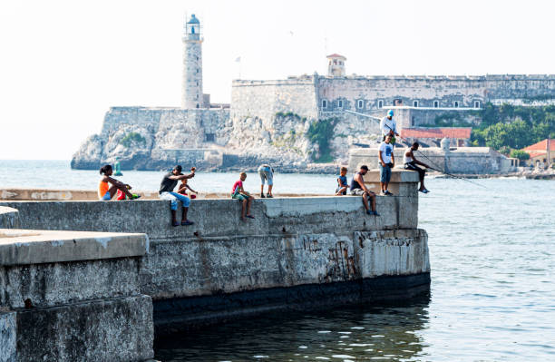 wędkarstwo siedząc na ścianie cementowej z zamkiem el moro w tle w hawanie kuba - capital cities retaining wall malecon coastline zdjęcia i obrazy z banku zdjęć