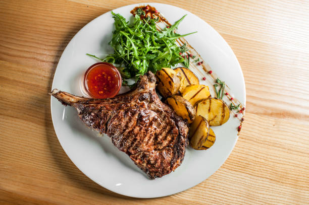 A juicy, appetizing steak, cooked on the grill, lies with vegetables and sauce on a white plate.