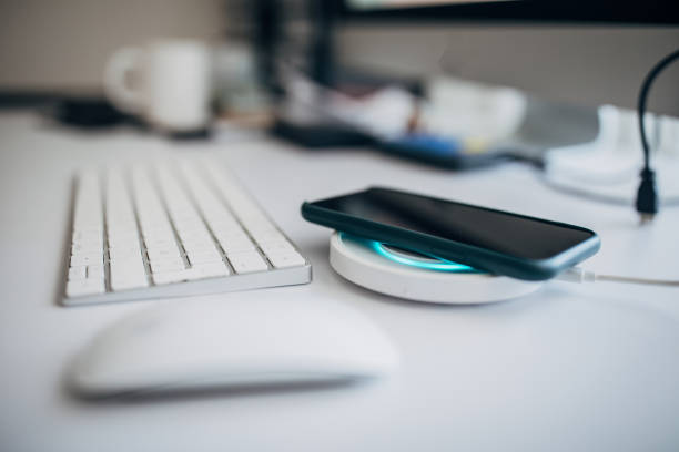 istock Smart phone charging on wireless phone charger next to computer keyboard in office 1203979730