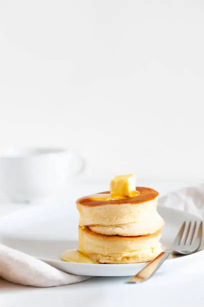 Fluffy Japan soufflé pancakes, hotcakes with butter and maple syrup or honey sauces on light white background with copy space. Trendy Asian food for breakfast. Vertical orientation