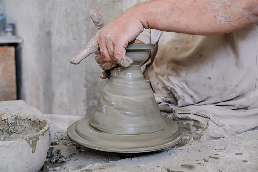 Close up shot of one man making pot using clay in pottery workshop class studio with pottery wheel