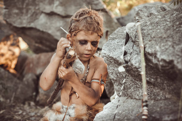 istock Caveman, manly boy making primitive stone weapon in camp 1203982952