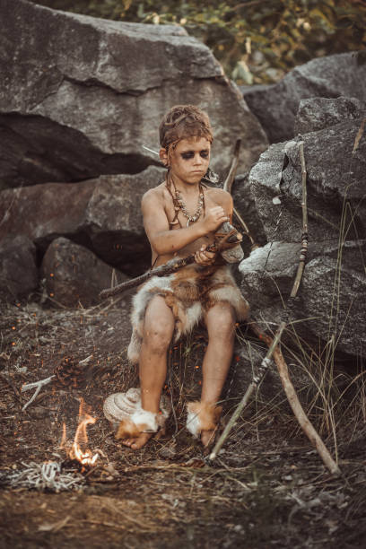 istock Caveman, manly boy making primitive stone weapon in camp 1203982978