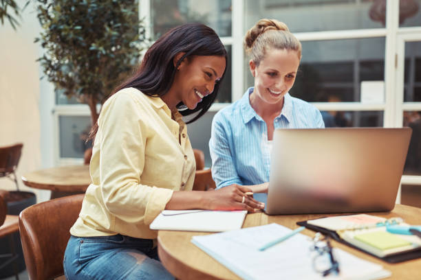 istock Laughing young businesswomen using a laptop in an office lounge 1203983689