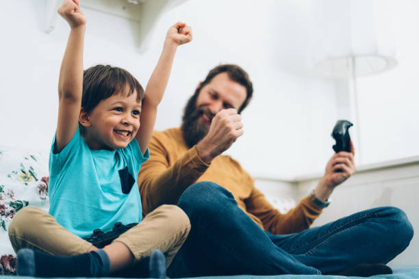 Father and son playing video games at home Little boy competing with his father on video games game controller photos stock pictures, royalty-free photos & images