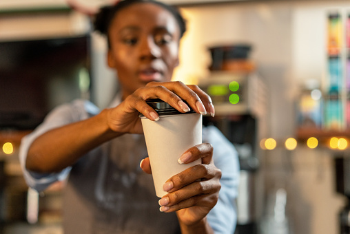 Close-up on a single-use coffee cup, as a barista places the plastic lid on top, at a cafe in San Francisco, California.