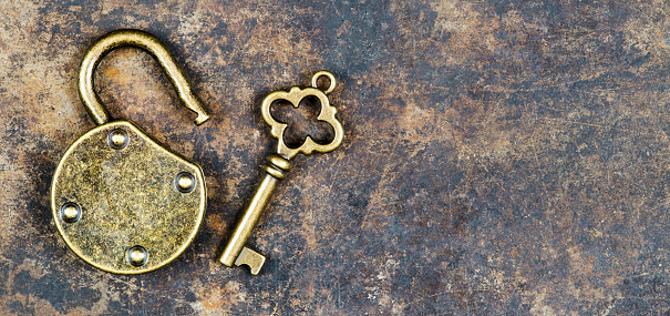 Escape room concept. Web banner of a vintage golden key and unlocked padlock on a rusty metal background.