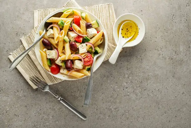 Pasta salad with feta cheese and vegetables on grey background. Greek salad with pasta.