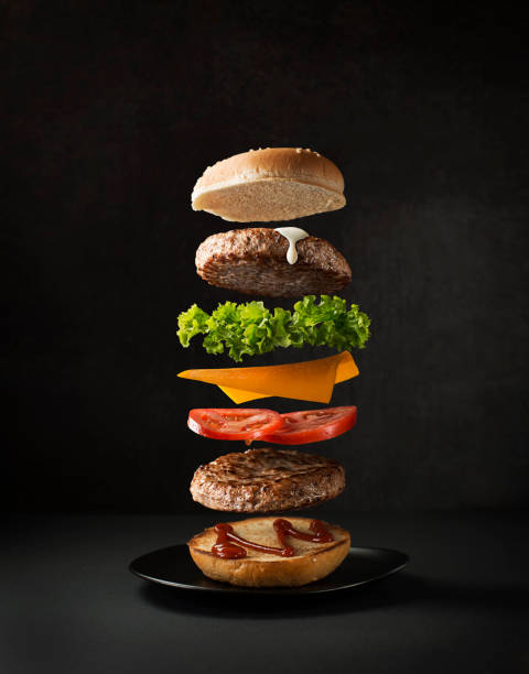 Hamburger with flying ingredients Maxi hamburger with flying ingredients placed on black background. Conceptual jumping Burger. Delicious and attractive hamburger with refreshing ingredients serving size photos stock pictures, royalty-free photos & images