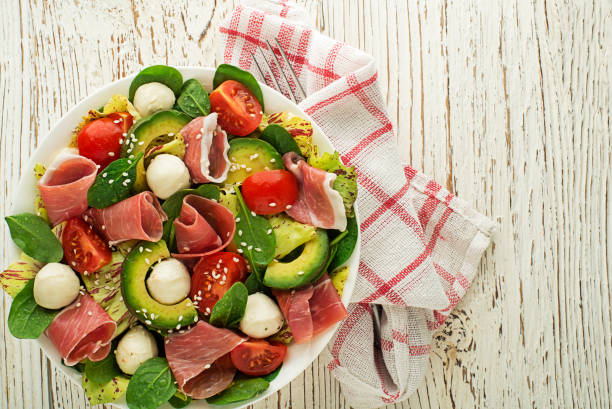 green salad with prosciutto Healthy green salad with prosciutto, avocado and mozzarella cheese on wooden table background. Healthy meal. salad fruit lettuce spring stock pictures, royalty-free photos & images