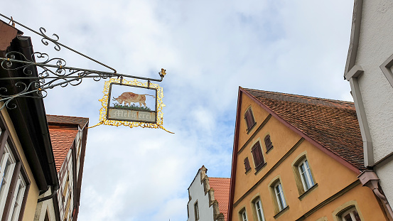 Rothenburg ob der Tauber - October 10, 2019 : Looking up at an antique forged signboard, hanging outside a butchery, different ancient house gables and a blue cloudy sky.
