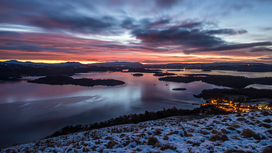 Sunrise on a cloudy, winter morning over the village of Luss and Loch Lomond as seen from the slopes of Beinn Dubh, Scotland.