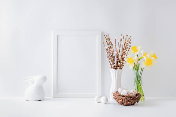 istock Home interior with easter decor. Mockup with a white frame and yellow daffodils in a glass vase on a light background 1203997278