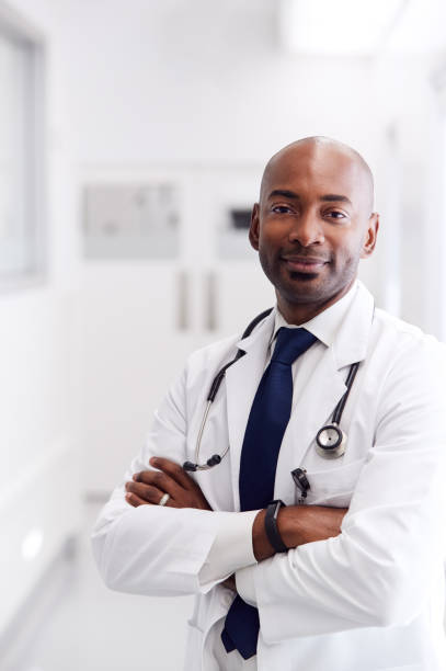 ritratto di medico maschio maturo che indossa il camice bianco in piedi nel corridoio dell'ospedale - mature adult men male african descent foto e immagini stock