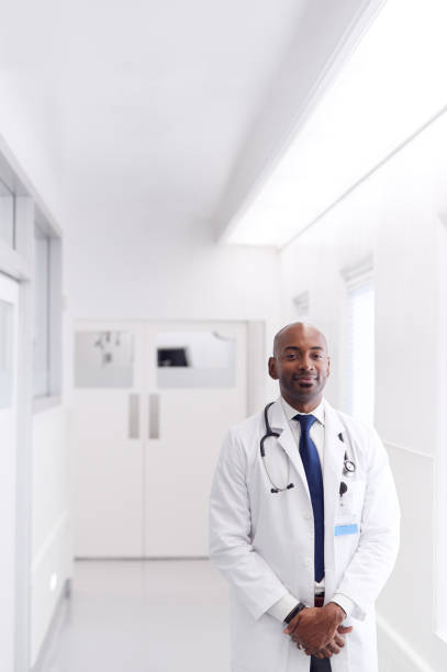 ritratto di medico maschio maturo che indossa il camice bianco in piedi nel corridoio dell'ospedale - doctor male doctor mature men portrait foto e immagini stock