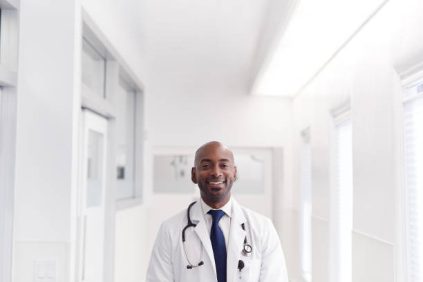 ritratto di medico maschio maturo che indossa il camice bianco in piedi nel corridoio dell'ospedale - doctor male doctor mature men portrait foto e immagini stock