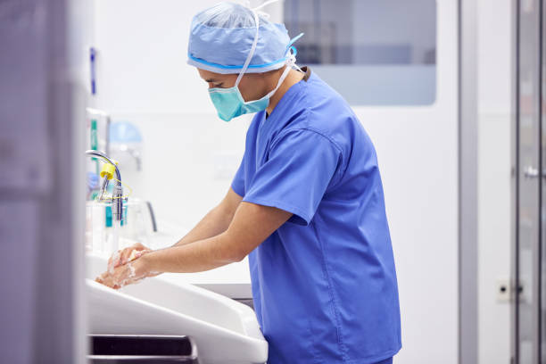 male surgeon wearing scrubs washing hands before operation in hospital operating theater - hand hygiene imagens e fotografias de stock