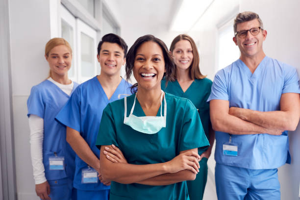 Portrait Of Laughing Multi-Cultural Medical Team Standing In Hospital Corridor Portrait Of Laughing Multi-Cultural Medical Team Standing In Hospital Corridor medical scrubs stock pictures, royalty-free photos & images